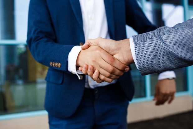 Picture of  two young businessmen on street background shake hands